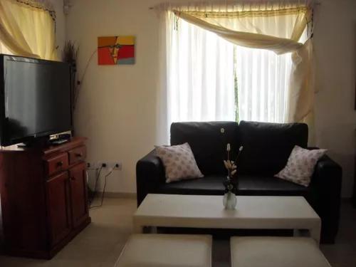 sala de estar con sofá negro y TV en Duplex en Alquiler con Pileta Privada Pinamar Valeria del Mar en Valeria del Mar