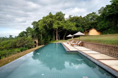 a swimming pool with a bench next to a field at Lunuganga Estate in Bentota