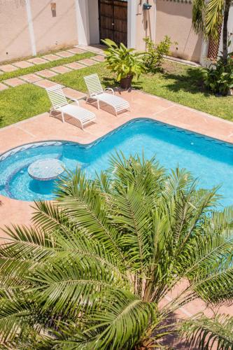 a swimming pool with two chairs and palm trees at Casa privada con alberca grande in Chetumal
