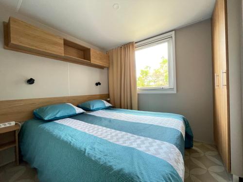 Un dormitorio con una cama con almohadas azules y una ventana en Camping le lac des rêves L'ABRIZEN, en Lattes