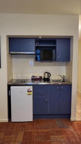a kitchen with blue cabinets and a white refrigerator at City of Sails Motel in Auckland