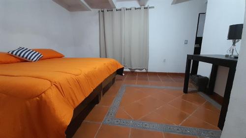 a bedroom with an orange bed and a table at Posada El Refugio in Mineral de Pozos