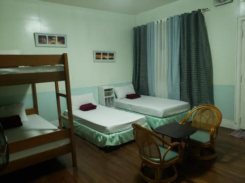 a room with two beds and a chair and a table at Old Orangewood Bed & Breakfast in Baguio
