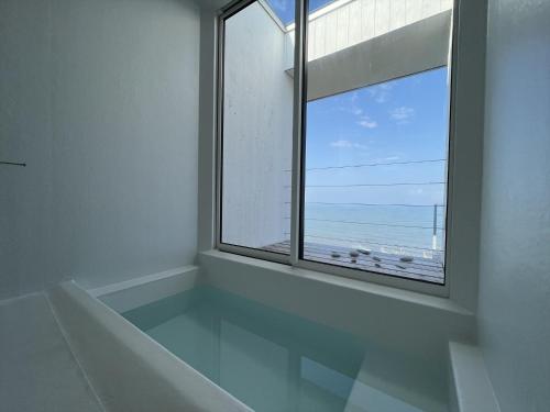 um quarto branco com uma grande janela e o oceano em Cliff House Morai em Ishikari