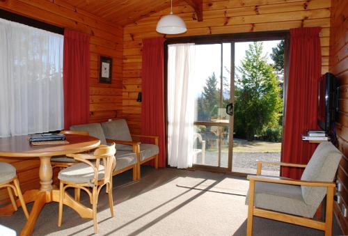 - un salon avec une table, des chaises et une grande fenêtre dans l'établissement The Chalets Motel, à Hanmer Springs