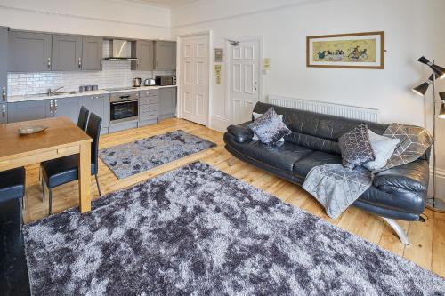 a living room with a black leather couch and a kitchen at Apartment 3, Khyber Lodge Apartments Whitby in Whitby