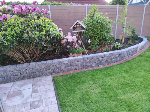 a garden with a stone wall and flowers and a bird house at Ferienwohnung Reddemann in Westerstede