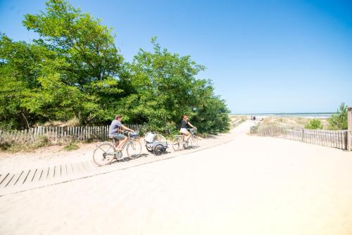 two people riding bikes down a road next to a fence at Villages Clubs du Soleil - RONCE LES BAINS in Ronce-les-Bains