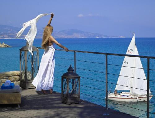 una donna in abito bianco su un balcone con una barca a vela di Paradisso Beach Villas ad Amoudi