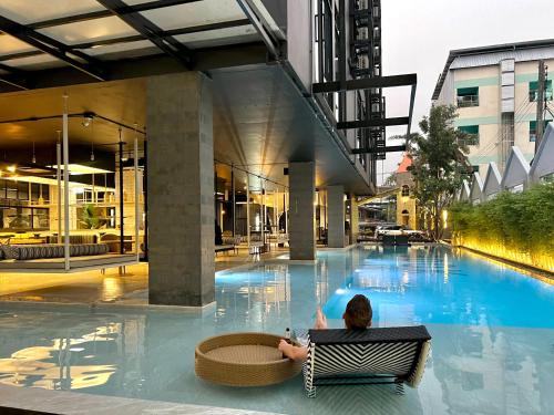 un hombre sentado en una silla frente a una piscina en BOOK Design HOTEL -SHA Extra Plus en Chiang Mai