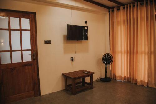 Ollie resort في إيلا: غرفة مع طاولة وتلفزيون على الحائط