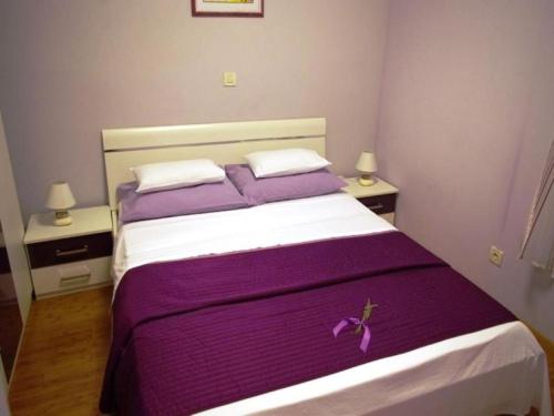 a bedroom with a large bed with purple sheets and pillows at Apartments Njoko - sea view in Prvić Šepurine