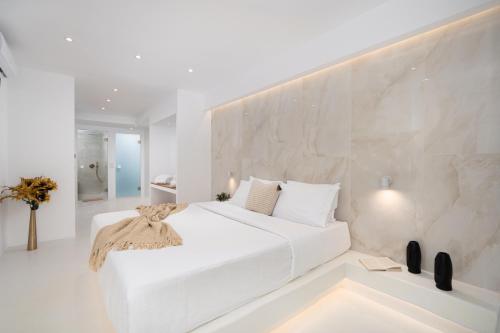 a white bedroom with a white bed and a stone wall at Cycladic Suites in Fira