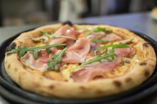 a pizza with ham and greens on a black plate at Hotel Roberto Slanic Prahova in Slănic