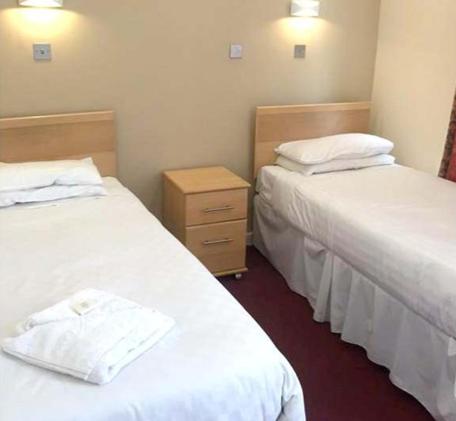 Hadleigh Hotel في إيستبورن: سريرين في غرفة الفندق ذات شراشف بيضاء