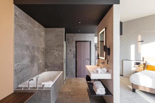 a bathroom with a bath tub and a bedroom at Mercure Namur Hotel in Namur