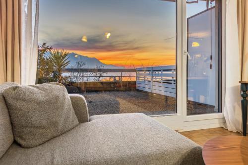 een woonkamer met een bank en een raam met een zonsondergang bij Beautiful Studio Lake View and Castle in Veytaux
