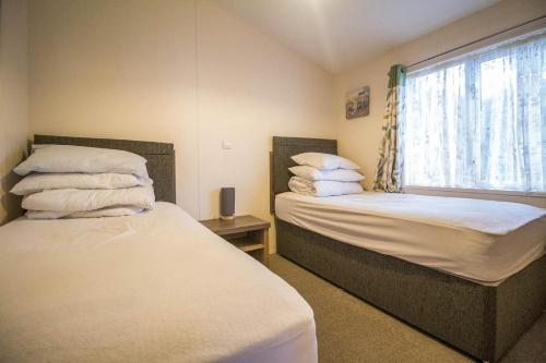 a bedroom with two beds and a window with pillows at Luxury Lodge With Full Sea Views At Azure Seas In Suffolk Ref 32105og in Lowestoft