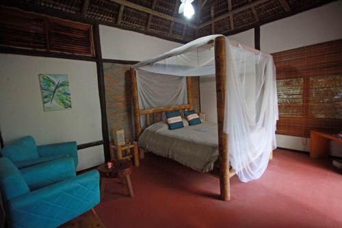 ein Schlafzimmer mit einem Himmelbett und einem blauen Stuhl in der Unterkunft Bambusada Boutique Hotel in Canavieiras