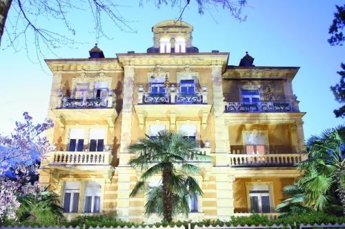 a large yellow building with a palm tree in front of it at Hotel Villa Westend in Merano