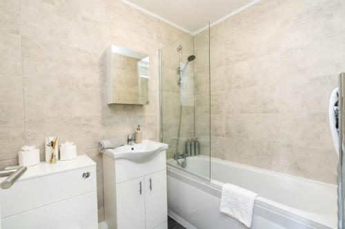 La salle de bains est pourvue d'un lavabo, d'une douche et d'une baignoire. dans l'établissement Sleek and Stylish 2BD Home with a Garden Anerley, à Londres