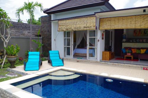 a house with a swimming pool and two blue chairs at Ratna Villa in Ubud