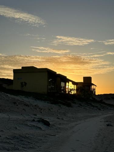 a building on the beach with the sunset in the background at Bangalô Encantador Praia da Baleia in Itapipoca