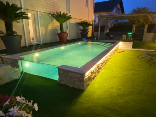 a swimming pool with lights in a backyard at night at Auberge des Sauterelles in Sermersheim