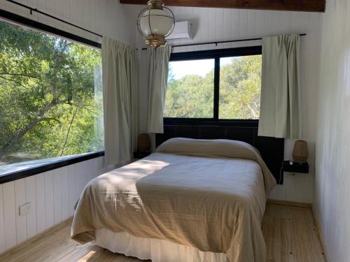 a bedroom with a bed and two large windows at Cabaña Los Lirios in Tigre