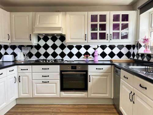 a kitchen with white cabinets and a black and white checkered wall at Bright, Airy & Beautifully Decorated 3 Bedroom Home in Kettering