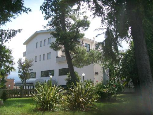 un bâtiment blanc avec des arbres et des plantes devant lui dans l'établissement Hotel Du Parc, à Atri