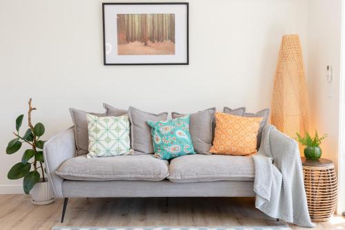 a living room with a gray couch with colorful pillows at Grace Road Getaway in Tauranga