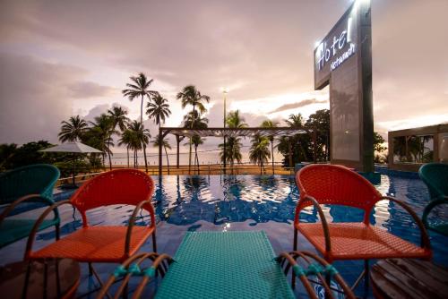uma piscina com duas cadeiras e uma mesa e uma placa em Netuanah Praia Hotel em João Pessoa