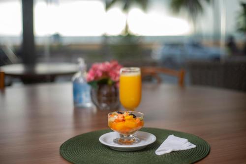 a glass of orange juice and a bowl of fruit on a table at Netuanah Praia Hotel in João Pessoa