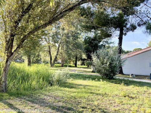 une cour avec des arbres et de l'herbe et un bâtiment dans l'établissement Maison rénovée 2023 à La Palmyre - Proche plage et commerces - 4 pers, terrasse et parking - FR-1-705-17, à La Palmyre