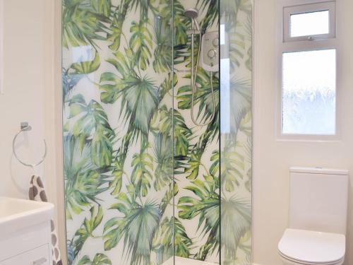 a bathroom with a shower with green palm trees wallpaper at Sanderling - Uk32837 in Hodgeston