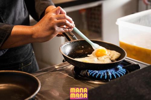 a person cooking an egg in a pan on a stove at Ceylonz KLCC by Mana-Mana in Kuala Lumpur