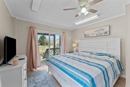 a bedroom with a bed with a ceiling fan and a window at The Sandy Eagle in Kill Devil Hills
