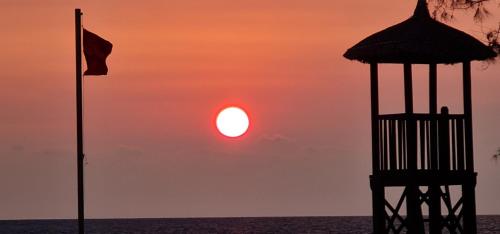 a sunset over the ocean with a pier and a flag at BREAKING DAWN- TAEYANG Hotel Phú Quốc in Phu Quoc