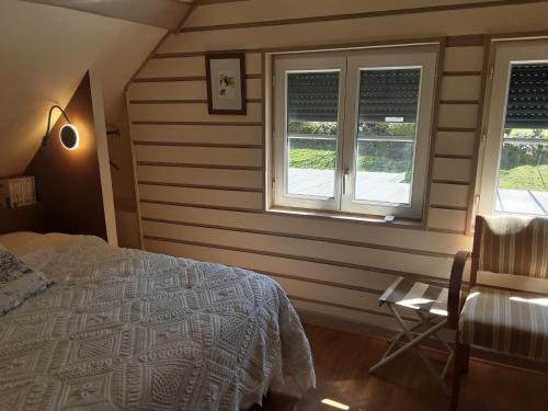sypialnia z łóżkiem, 2 oknami i krzesłem w obiekcie Le Clos du Buisson w mieście Saint-Julien-de-la-Liègue