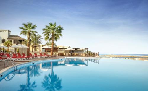 a large swimming pool with chairs and palm trees at Peaceful Private Villa at Five Star Beach Resort in Ras al Khaimah