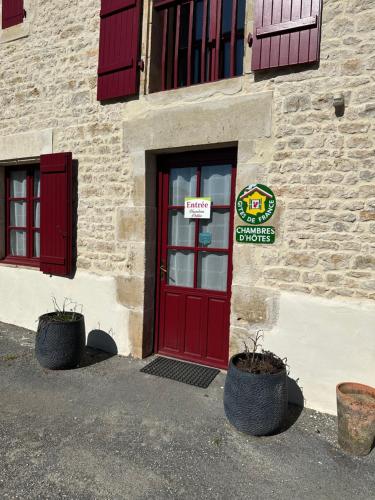 a red door of a building with two plants in front at Chambres d'hôtes du puy d'anché in Sauzé-Vaussais