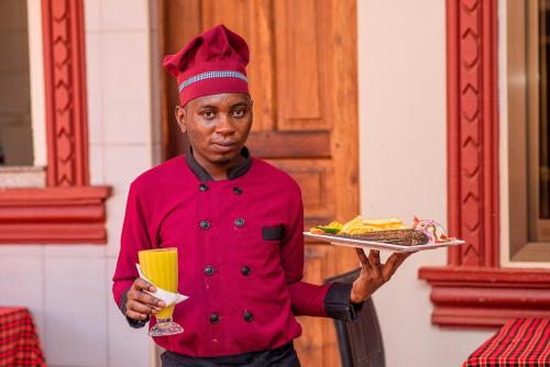 a chef holding a tray of food and a drink at Spring Hills Hotel - Morogoro in Morogoro