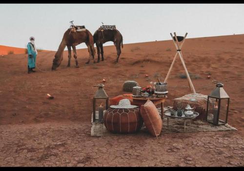 a desert with a table and a camel in the desert at Merzouga best camp in Merzouga
