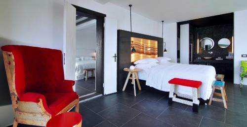 a bedroom with a white bed and a red chair at Myconian Avaton, a Member of Design Hotels in Elia Beach