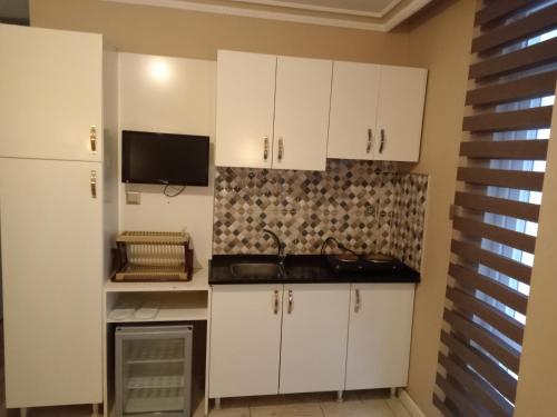 a kitchen with white cabinets and a tv on the wall at Send Apart Otel in Antalya