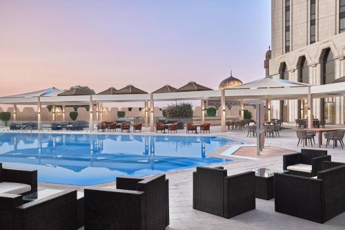 basen ze stołami i krzesłami oraz budynek w obiekcie Riyadh Airport Marriott Hotel w Rijadzie