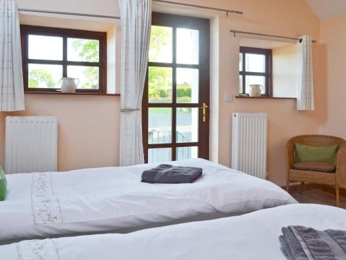 two beds in a bedroom with windows and a chair at The Granary- Osc in Penbryn