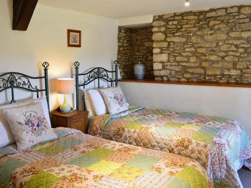 a bedroom with two beds and a stone wall at Rose Cottage in Cold Ashton