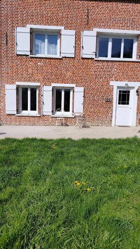 a brick building with white windows and a grass field at les jardins d'Holly in Avesnes-en-Bray